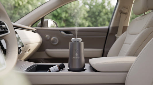 ARONIQ autodiffuser in de bekerhouder met een dunne nevel en een flesje olie uit de zon